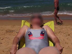 Зрелая женщина в купальнике лежит на пляже и отдыхает попав под камеру